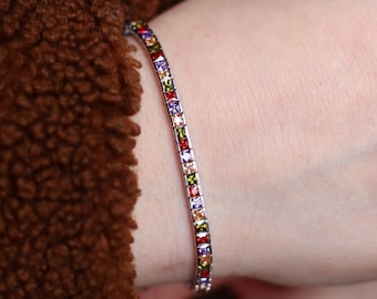 Può includere: Un bracciale tennis color argento caratterizzato da una fila continua di pietre preziose a taglio quadrato multicolore nelle tonalità del rosso, viola, arancione e verde. Il bracciale è realizzato con una montatura a maglie metalliche.