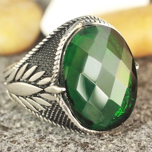 May include: A silver ring with a large, faceted, green gemstone. The ring has a detailed design with leaf-like accents.