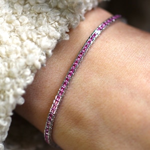 Pode incluir: Um bracelete delicado com uma corrente de prata e pedras quadradas cor-de-rosa.