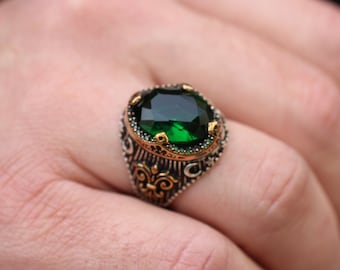 May include: A silver ring with an ornate design and a large, oval-shaped green gemstone.