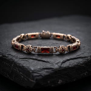 May include: A metallic bracelet featuring alternating rectangular and ornate circular links. The rectangular links are set with deep red baguette-cut stones, while the circular links contain small, round red stones. The metal has a dark, antique finish.