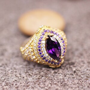 May include: A gold ring with a large purple marquise-shaped gemstone surrounded by smaller purple and white gemstones.