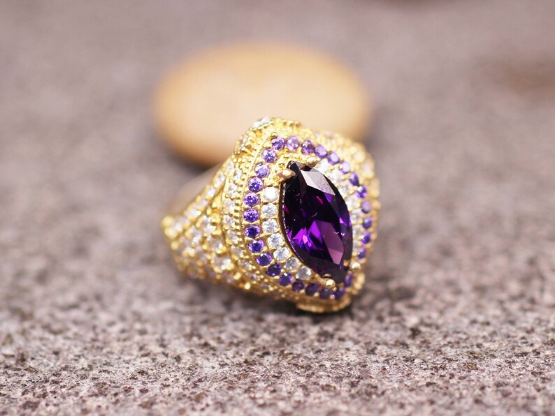 May include: A gold ring with a large purple marquise-shaped gemstone surrounded by smaller purple and white gemstones.