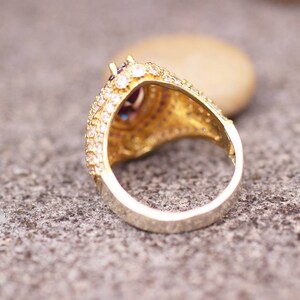 May include: A gold ring with a large, faceted, purple gemstone surrounded by smaller clear gemstones. The ring is set in a filigree design.