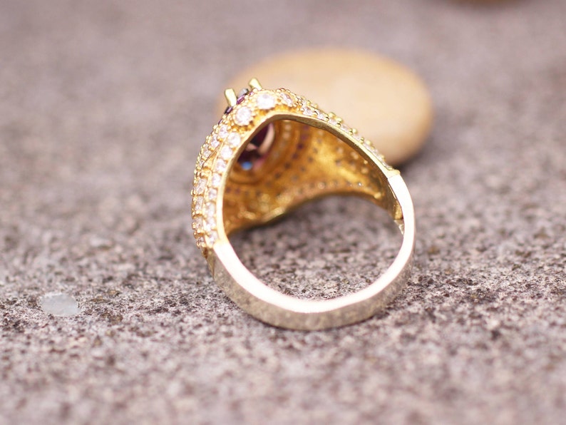 May include: A gold ring with a large, faceted, purple gemstone surrounded by smaller clear gemstones. The ring is set in a filigree design.