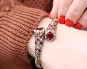 Pode incluir: Um bracelete de ouro com duas pedras preciosas vermelhas e pedras preciosas rosadas menores engastadas em um design floral.