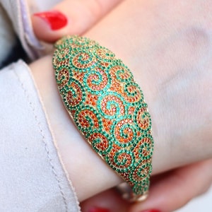 May include: A gold bangle bracelet with a swirling pattern of green and orange gemstones.