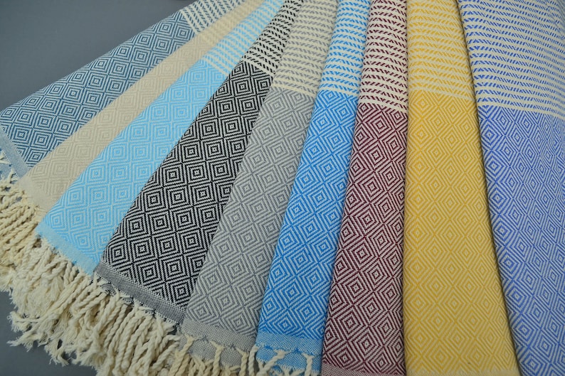 Pu&ograve; includere: Una collezione di asciugamani turchi in vari colori e motivi, tra cui blu, giallo, grigio e nero. Gli asciugamani hanno un motivo a rombi e bordi con frange.