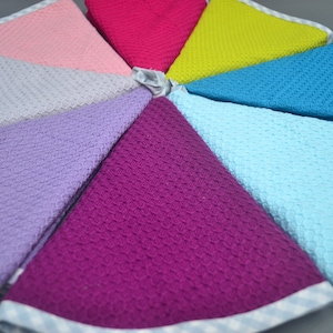 Puede incluir: Un juego de ocho toallas de cocina de tejido de gofre en varios colores, incluyendo rosa, morado, azul claro, turquesa, verde y rojo. Las toallas tienen un ribete a cuadros blanco y azul.