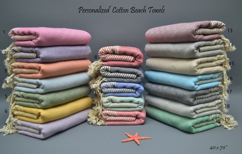 Pu&ograve; includere: Una pila di 19 asciugamani da spiaggia in cotone personalizzati in vari colori, tra cui rosa, viola, arancione, blu, verde, giallo e grigio. Gli asciugamani sono piegati e impilati in due file, con i numeri da 1 a 7 a sinistra e da 8 a 19 a destra. Gli asciugamani misurano 40 pollici per 70 pollici.