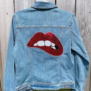 May include: A blue denim jacket with a red sequined lips patch on the back.