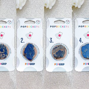Könnte beinhalten: Vier Handygriffe mit einem blauen und goldenen Marmormuster. Jeder Griff ist mit einer Nummer von 1 bis 4 und den Worten "POPSOCKETS" und "POPGRIP" gekennzeichnet.