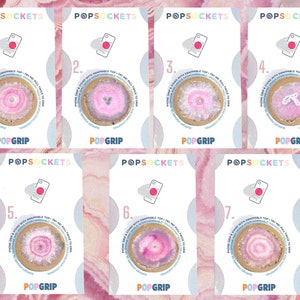Könnte beinhalten: Sieben verschiedene Handygriff-Designs mit rosa und weißen Achat-Scheiben mit goldenen Akzenten. Jedes Design ist mit einer Nummer von 1 bis 7 gekennzeichnet. Die Handygriffe befinden sich alle auf weißen Karten mit den aufgedruckten Wörtern "POPSOCKETS" und "POPGRIP".