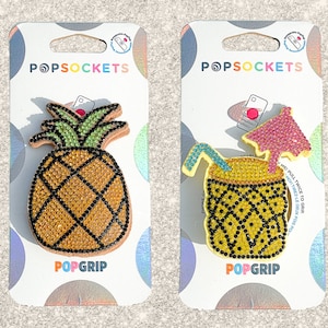 May include: Two PopSockets phone grips, one with a yellow pineapple design and the other with a yellow and black pineapple drink design. Both grips have the words "PopGrip" and "PopSockets" printed on them.