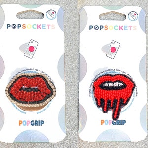Puede incluir: Dos agarres para teléfono PopSockets con tapas intercambiables. El primer agarre presenta un diseño de labios rojos con cuentas y un contorno negro y diamantes de imitación. El segundo agarre presenta un diseño de labios rojos con cuentas que gotean con un contorno negro.