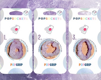 May include: Three phone grip packaging cards with the brand name "POPSOCKETS" and "POPGRIP" printed on them. Each card features a different purple and gold geode design with a pink phone icon on the top.