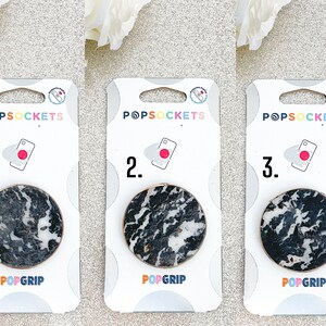 Könnte beinhalten: Drei weiße Kartenverpackungen für PopSockets-Handygriffe. Jede Karte zeigt einen PopGrip im schwarz-weißen Marmormuster mit einem goldenen Ring. Die Karten sind mit 1, 2 und 3 nummeriert.