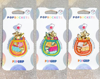 May include: Three colorful phone grips with a beaded design featuring a flower and a fruit. The grips are packaged on white cards with the text "POPSOCKET" and "POPGRIP".