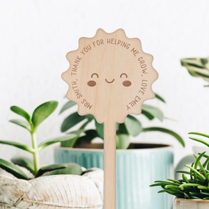 May include: Wooden plant stake with a smiling sun design and the text "Thank you for helping me grow, love Emily, Mrs. Smith".