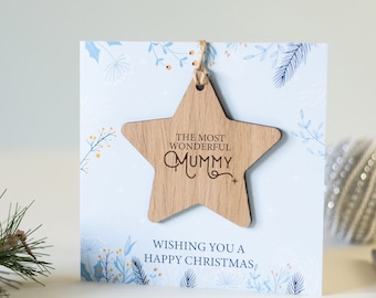 May include: A wooden star ornament with the text "The Most Wonderful Mummy" on a blue and white card with a floral design. The card reads "Wishing you a Happy Christmas".