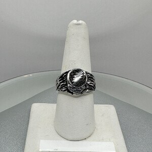 May include: A silver ring with a textured design featuring a raised oval-shaped stone. The ring is displayed on a white ring stand.