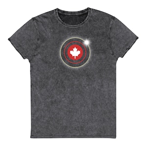 Può includere: Una t-shirt nera con un aspetto vissuto che presenta una bandiera canadese rossa e bianca all'interno di un cerchio con un contorno dorato.