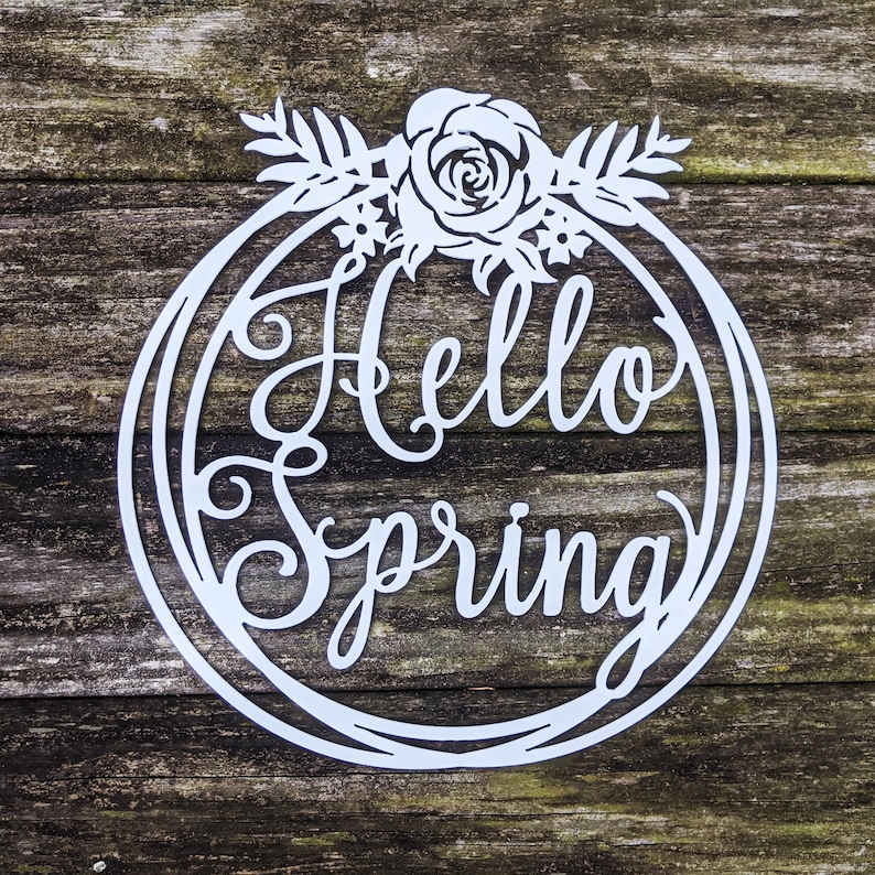 Pu&ograve; includere: Un cartello in metallo bianco con una ghirlanda di fiori e il testo "Hello Spring" in un carattere decorativo.