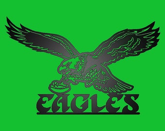May include: Black and white silhouette of an eagle with its wings spread, holding a football in its talons. The word "EAGLES" is written below the eagle in a stylized font.