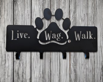 May include: Black metal key hook with three hooks. The hook is shaped like a paw print with the words "Live. Wag. Walk." on it.