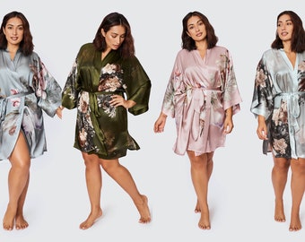 May include: Four women are wearing different colored silk robes with floral patterns. The robes are tied at the waist and have long sleeves. The women are standing in front of a white background.