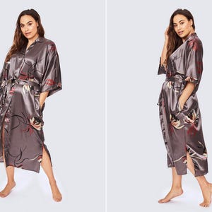 May include: A gunmetal gray satin robe featuring a floral print with red and white accents. The robe has a notched collar, wide three-quarter length sleeves, a matching tie belt at the waist, and side slits at the hem. The text HANA and GUNMETAL appear.