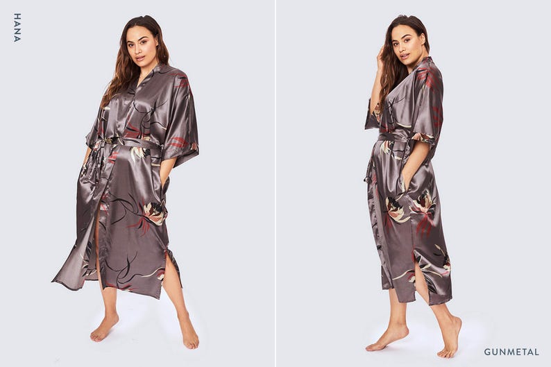 May include: A gunmetal gray satin robe featuring a floral print with red and white accents. The robe has a notched collar, wide three-quarter length sleeves, a matching tie belt at the waist, and side slits at the hem. The text HANA and GUNMETAL appear.