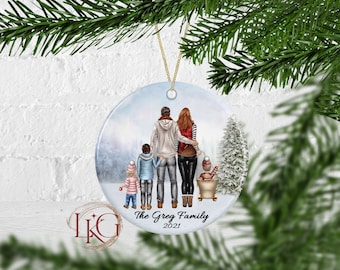 May include: A round Christmas ornament with a family illustration in a winter scene. The ornament features a family of four, with the text "The Greg Family 2021". It is hanging from a gold string.