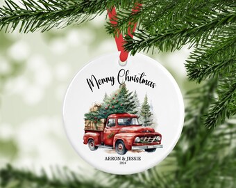 May include: White ceramic Christmas ornament with a red ribbon. The ornament features a watercolor illustration of a red vintage truck carrying a Christmas tree and gifts. Text reads "Merry Christmas" and a name and year.