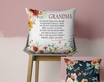 May include: A white throw pillow with floral designs and the word "GRANDMA" in burgundy. The pillow has a poem printed on it, surrounded by colorful flowers and butterflies. A second pillow with a dark background and floral design is also visible.