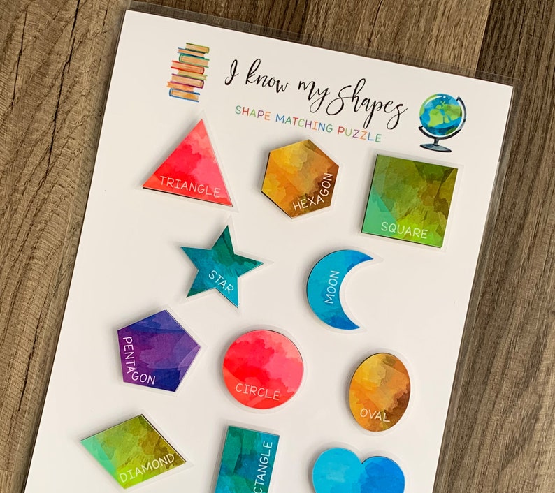 May include: A white card with the text "I know my shapes" and "Shape Matching Puzzle" printed on it. The card has 12 colorful shapes with their names printed on them, including a triangle, hexagon, square, star, moon, pentagon, circle, oval, diamond, and rectangle.