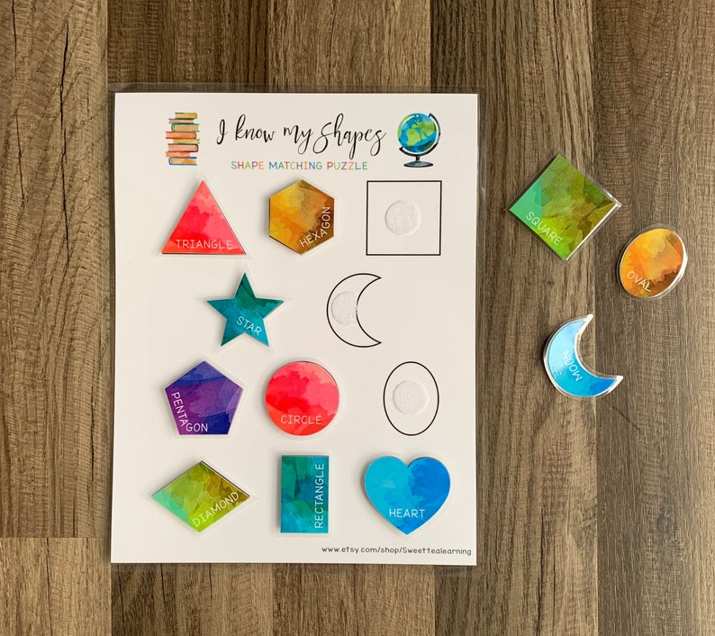 May include: A colorful educational shape matching puzzle for kids. The puzzle features a variety of shapes, including a triangle, square, circle, star, heart, hexagon, oval, crescent moon, diamond, rectangle, and pentagon. Each shape is labeled with its name.