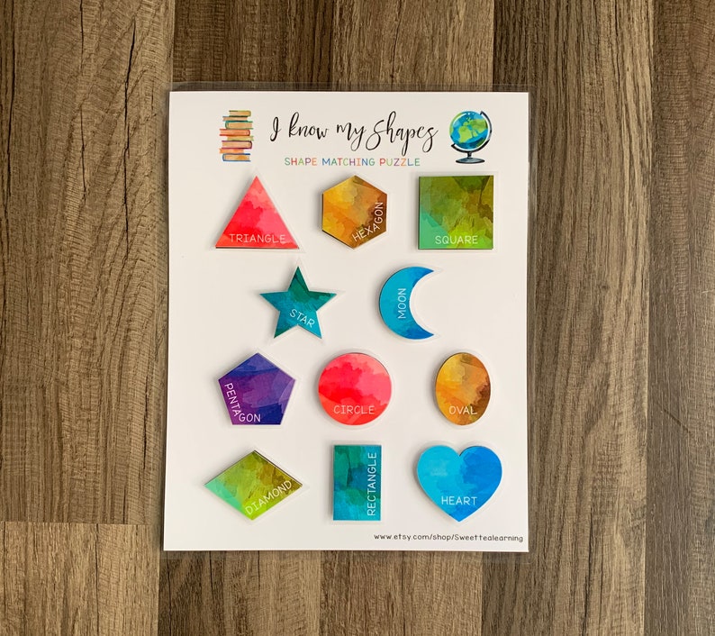 May include: A colorful wooden shape matching puzzle with 12 different shapes, including a triangle, hexagon, square, star, moon, pentagon, circle, oval, diamond, rectangle, and heart. The puzzle is labeled "I know my shapes" and "Shape Matching Puzzle".