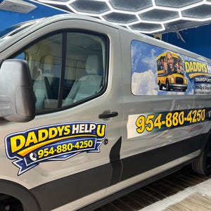 May include: A silver passenger van featuring custom vinyl decals for Daddys Help U Transportation. The side displays a yellow school bus graphic with a person, the company name, and the phone number 954-880-4250 in bold yellow and blue text.