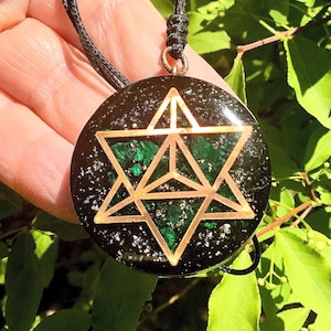 May include: Circular pendant with a black base, speckled with white and green. A copper-coloured Star of David design is set over a textured green area. The pendant is suspended from a black cord.