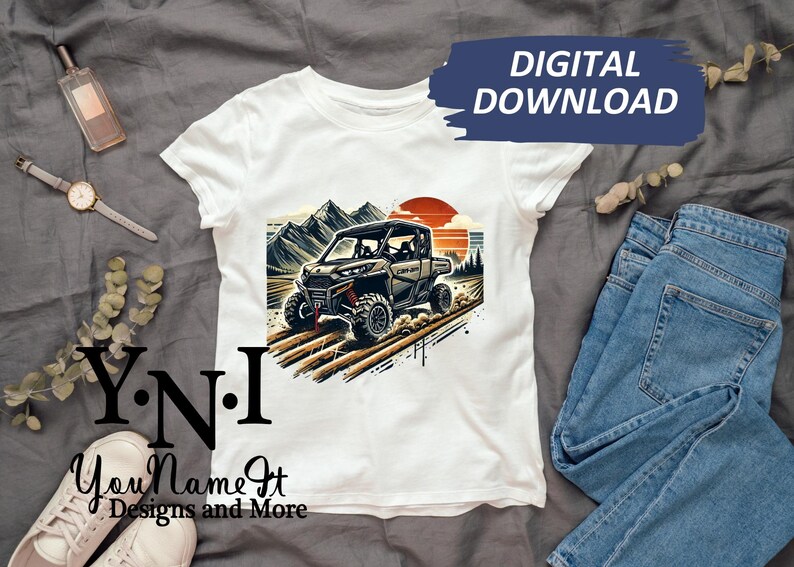 May include: White t-shirt with a graphic of a green and brown off-road vehicle driving through a mountain landscape. The text "Y.N.I. You Name It Designs and More" is printed on the bottom of the shirt.