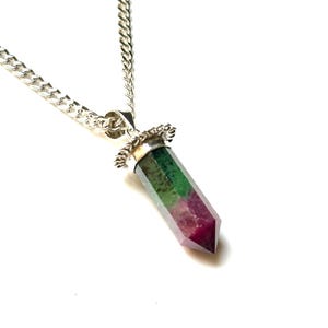 May include: A silver chain necklace with a pendant featuring a multi-colored crystal. The crystal is a mix of green, red, and clear colors, cut into a hexagonal shape. The pendant is attached to the chain with a decorative silver bail.