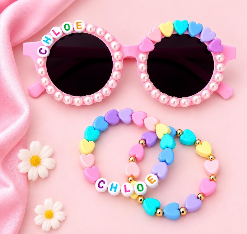 May include: Pink sunglasses decorated with white faux pearls and the name CHLOE in white letter beads on the left lens, plus two elastic bracelets featuring colorful heart-shaped beads, gold-tone spacers, and the name CHLOE in white letter beads.