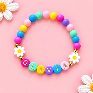 Peut inclure: Un bracelet circulaire composé de perles rondes colorées dans des tons rose, bleu, jaune, vert et violet. Le bracelet comprend des perles en forme de marguerite blanche avec un centre jaune, des perles intercalaires dorées et des perles épelant OLIVIA.
