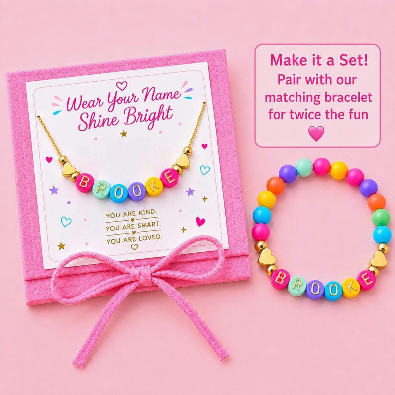 May include: A gold-tone chain necklace with colorful letter beads spelling BROOKE and gold heart charms on a pink display card with the text Wear Your Name Shine Bright, alongside a matching colorful beaded bracelet with the name BROOKE.
