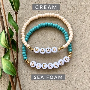 Pu&ograve; includere: Due braccialetti elastici composti da piccole perline rotonde. Un braccialetto &egrave; color crema, l'altro verde schiuma di mare. Il braccialetto crema presenta perline bianche che compongono la scritta MAMA in lettere dorate. Il braccialetto verde presenta perline bianche che compongono la scritta BLESSED in lettere dorate, con piccole perline metalliche dorate.