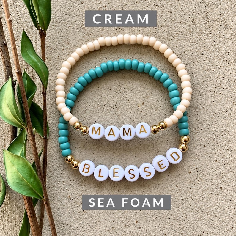 Pu&ograve; includere: Due braccialetti elastici composti da piccole perline rotonde. Un braccialetto &egrave; color crema, l'altro verde schiuma di mare. Il braccialetto crema presenta perline bianche che compongono la scritta MAMA in lettere dorate. Il braccialetto verde presenta perline bianche che compongono la scritta BLESSED in lettere dorate, con piccole perline metalliche dorate.