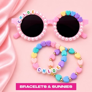 May include: Pink sunglasses with round black lenses, decorated with white faux pearls and the name CHLOE in colorful letter beads on the left frame, plus two heart-shaped bead bracelets featuring the name CHLOE and small gold-tone spacer beads.