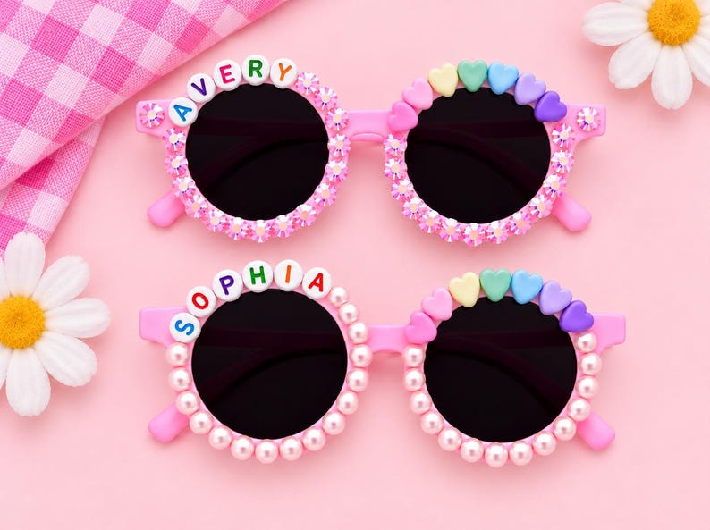 May include: Two pairs of pink sunglasses with round black lenses. The top pair features the name AVERY in colorful letter beads and pink crystals. The bottom pair features the name SOPHIA in colorful letter beads and white pearl-like beads.