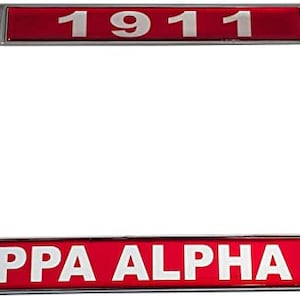 May include: A silver metal license plate frame with a red background and white text. The text reads "1911" on the top and "KAPPA ALPHA PSI" on the bottom.